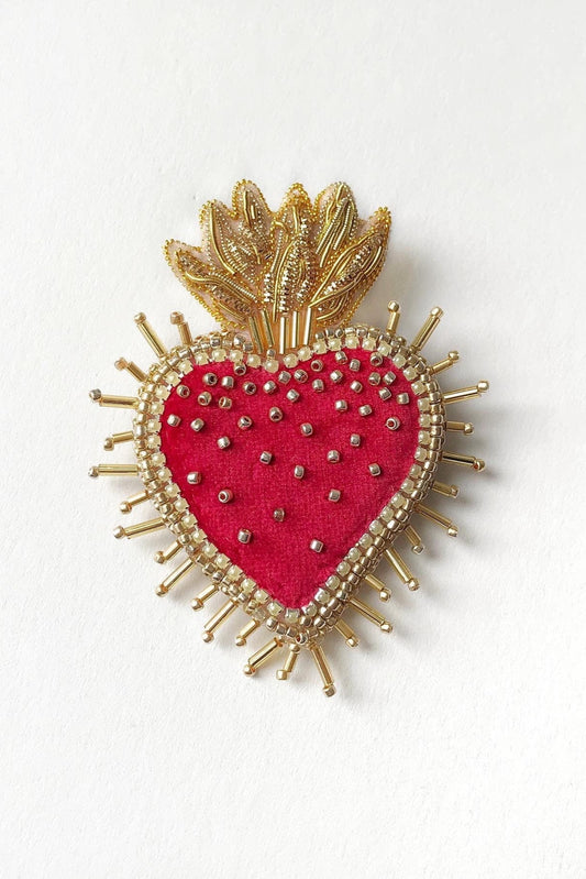 Heart-shaped brooch with gold detailing and red center on a white background
