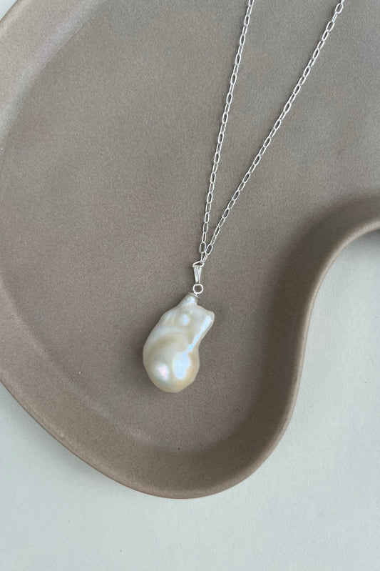 Pearl necklace on a silver chain displayed on a beige ceramic dish.
