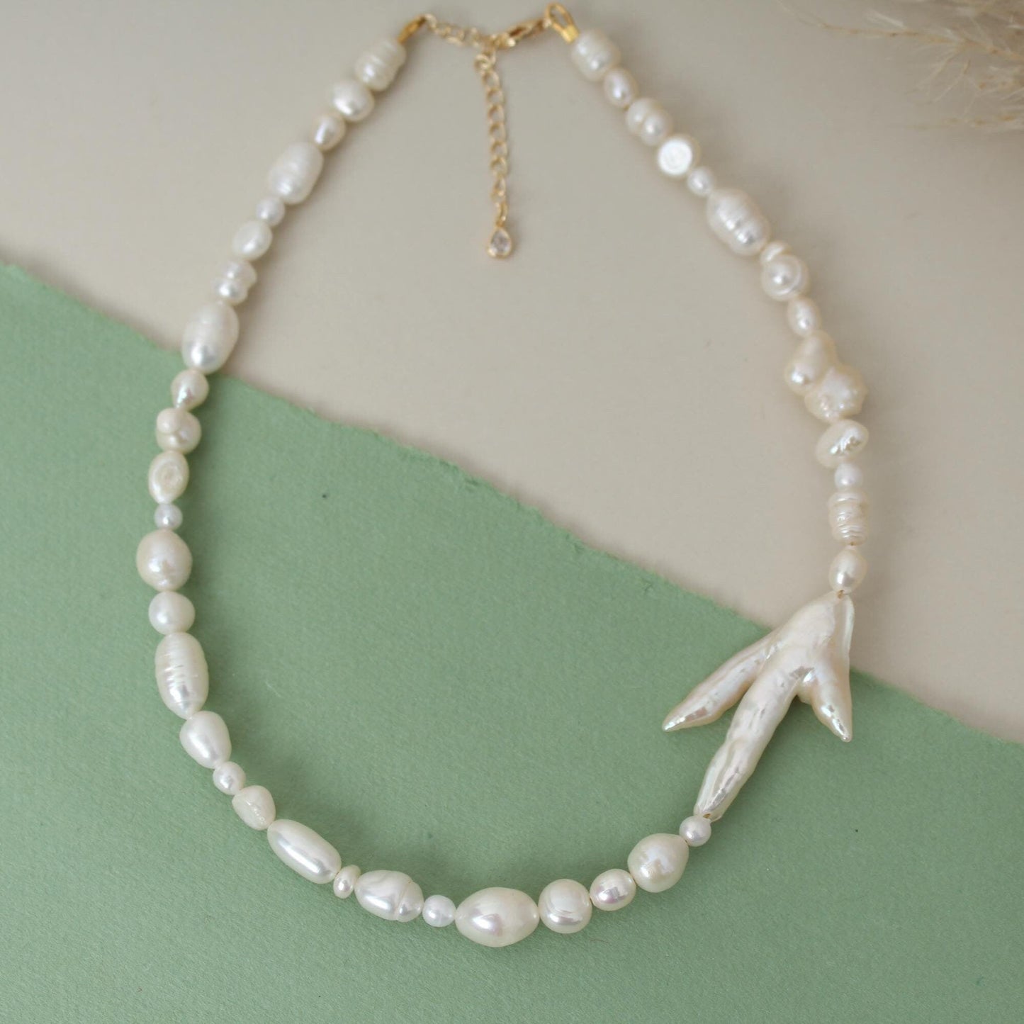 Pearl necklace with a leaf-shaped pendant on a green and beige background
