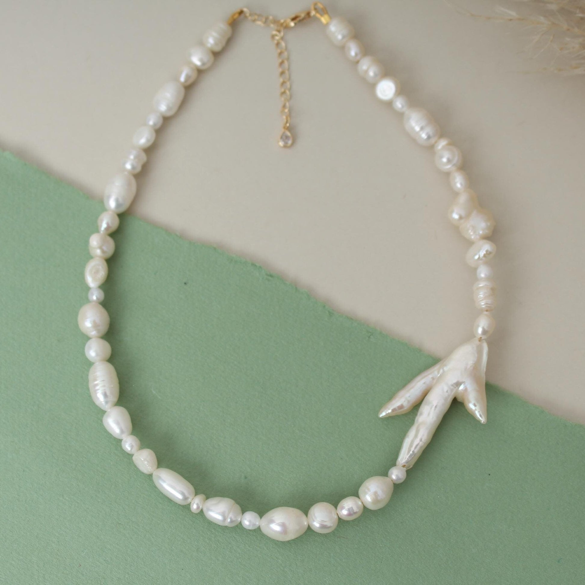 Pearl necklace with a leaf-shaped pendant on a green and beige background