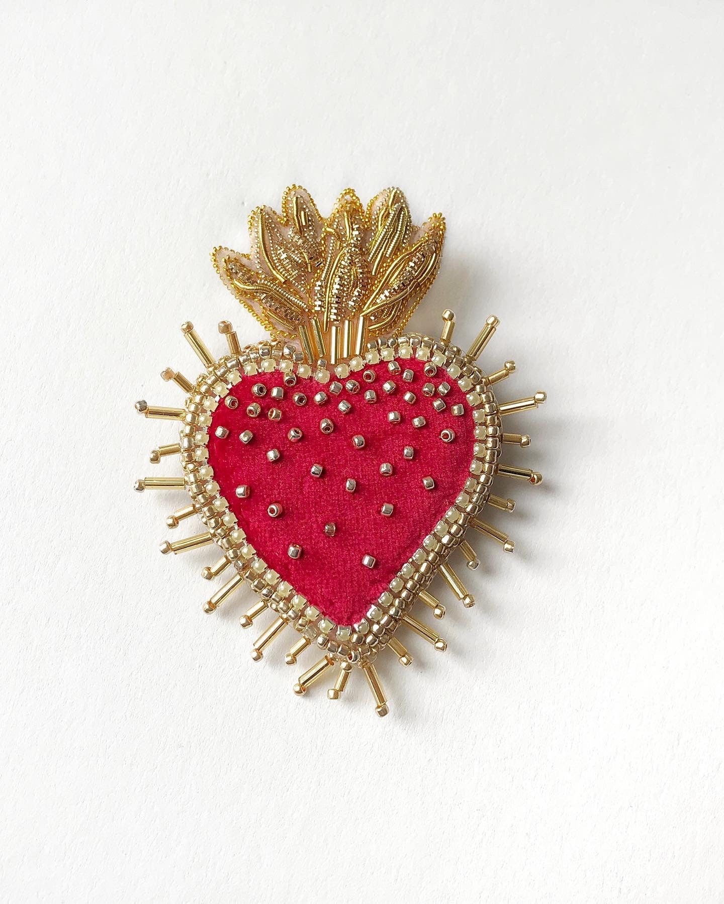 Heart-shaped brooch with gold detailing and red center on a white background