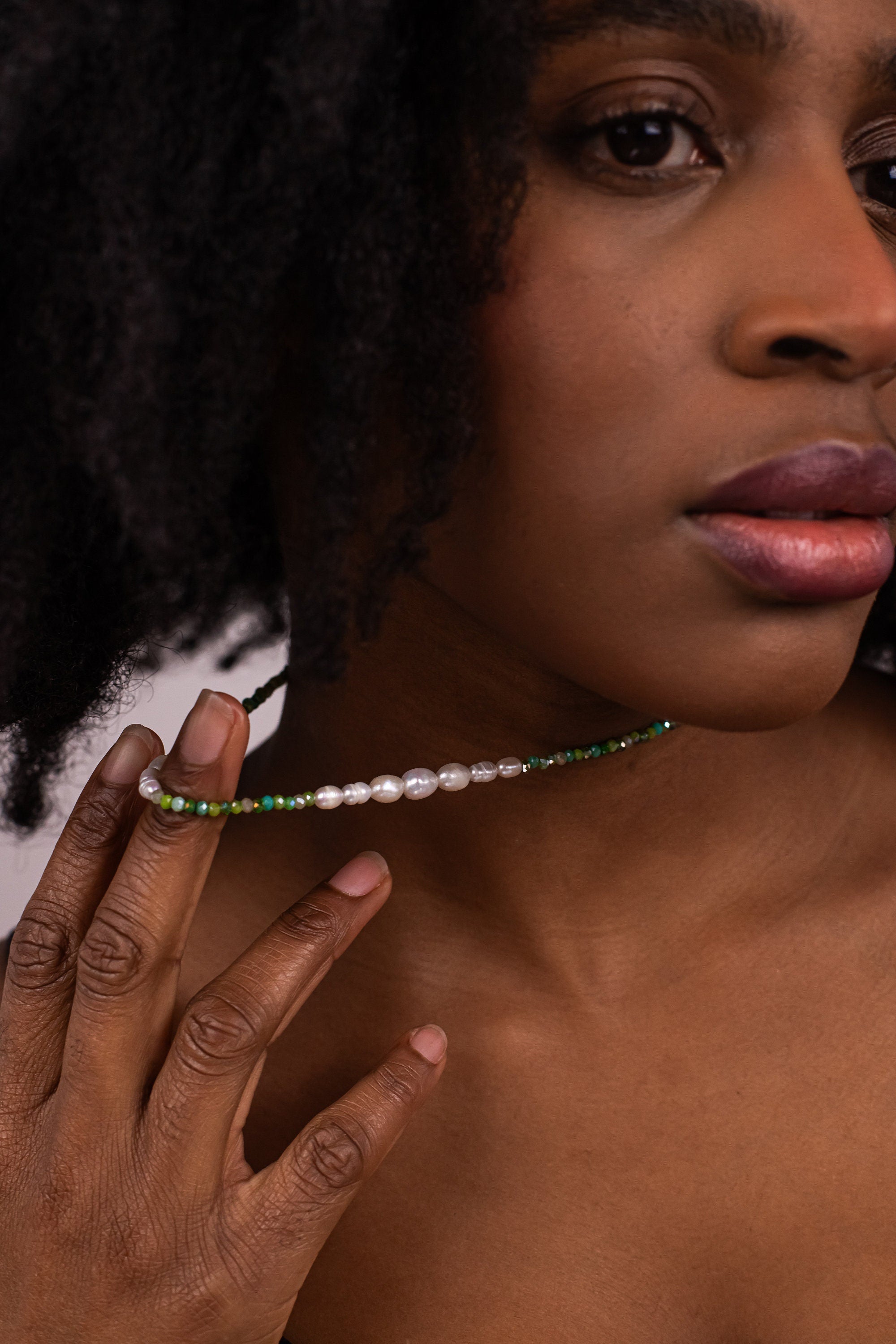 Woman wearing a necklace with a close-up of her hand and face.