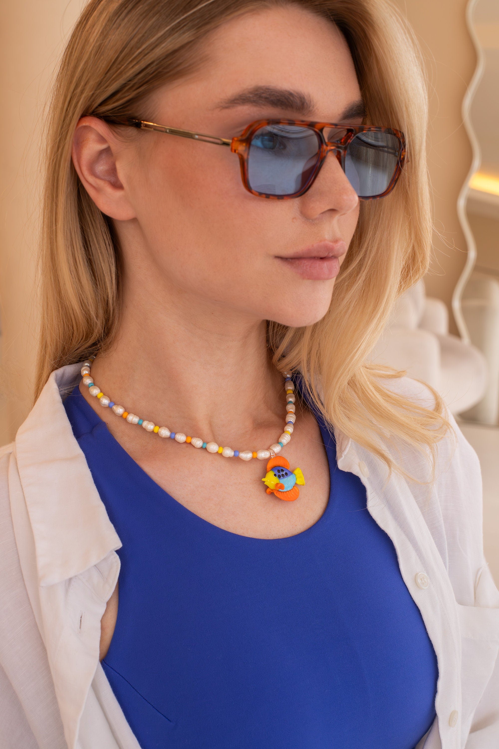 Woman wearing sunglasses and a colorful necklace with a blue top.