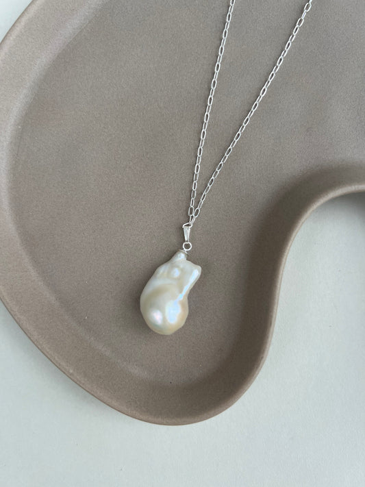 Pearl necklace on a silver chain displayed on a beige ceramic dish.