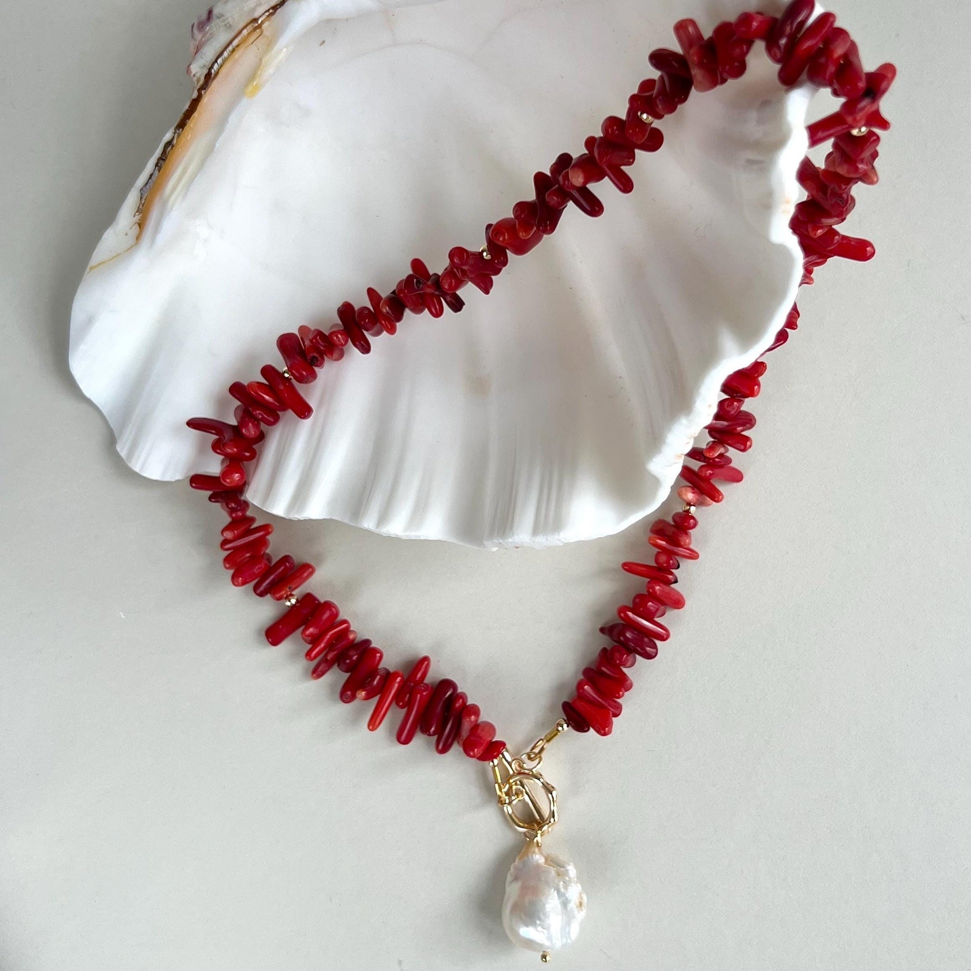 Red coral necklace with a pearl pendant on a white shell background