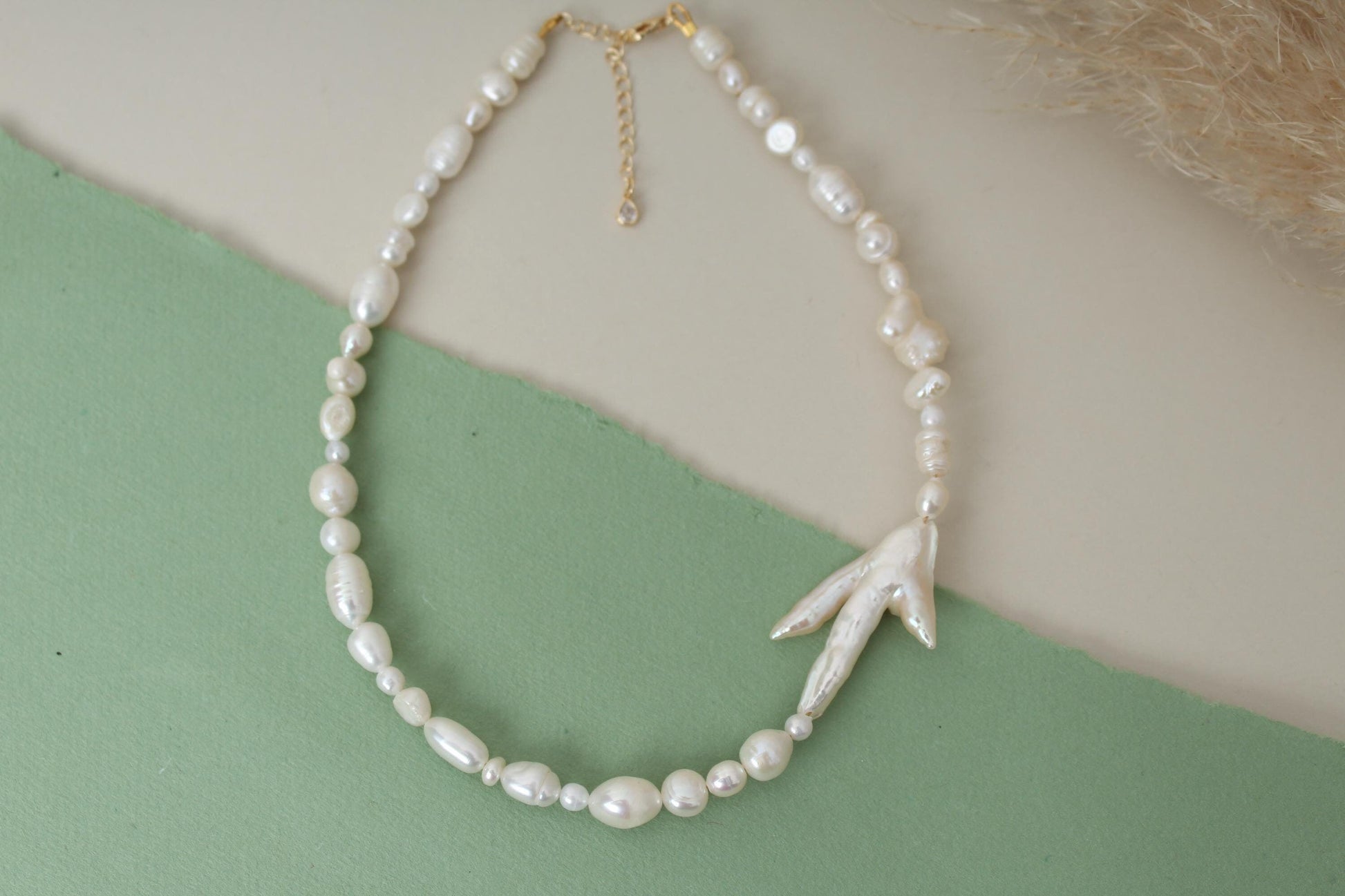 Pearl necklace with a leaf-shaped pendant on a green and beige background
