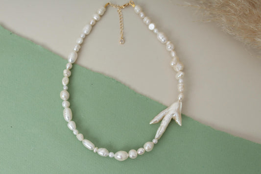 Pearl necklace with a leaf-shaped pendant on a green and beige background