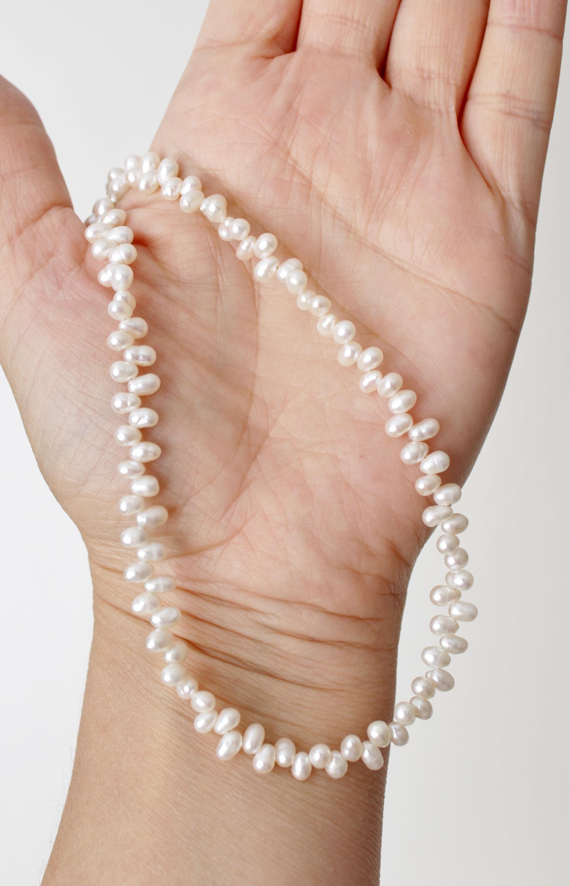 Pearl necklace held in a hand against a plain background